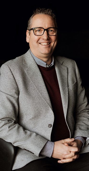 Man in grey blazer seated.